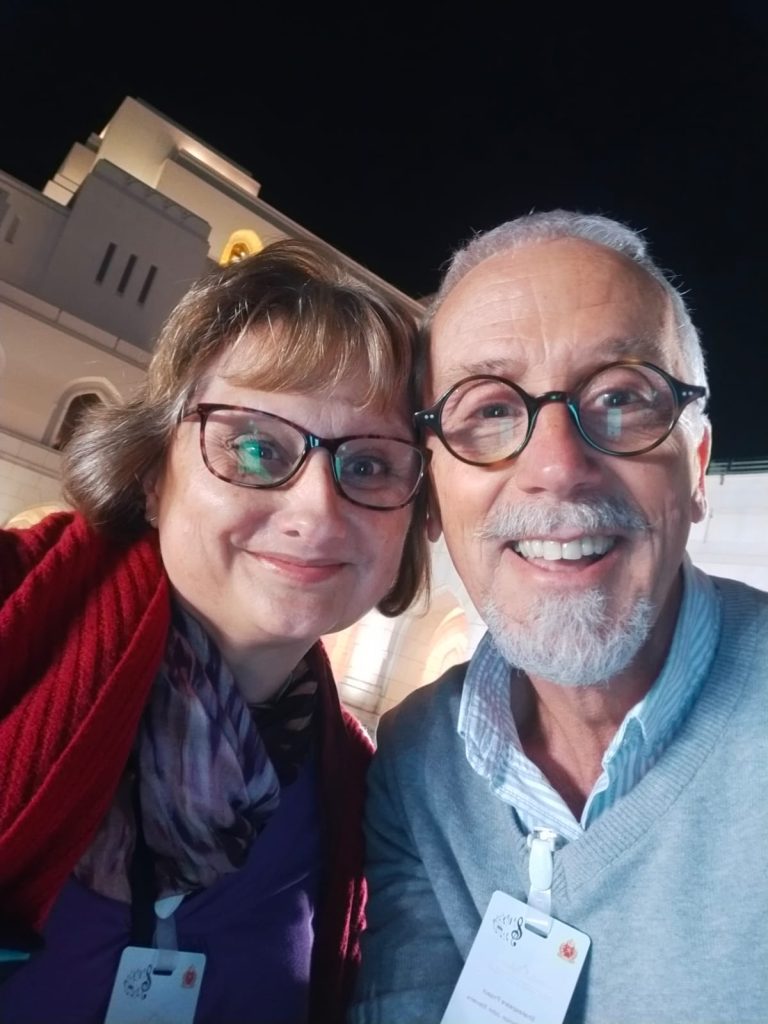 Jules and Richard outside the Royal Opera House, Oman in 2024. Dark background, both smiling. Head and shoulders only. 