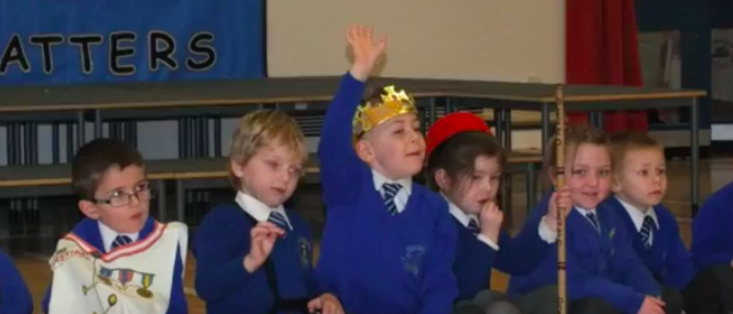 Group of KS1 children, some wearing workshop costumes, concentrating. One wearing a crown with his hand up to answer a question. 